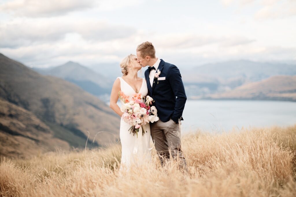 A bride and groom sharing a kiss atop Queenstown hill, overlooking Lake Wanaka during their heli-wedding.